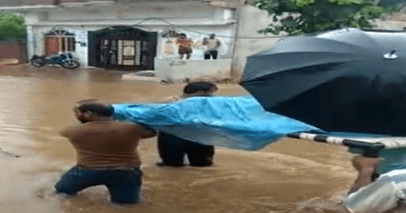 Family carries pregnant woman on cot, wades through knee-deep water